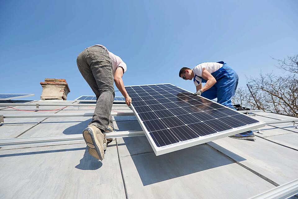 Arbeiter montieren eine Photovoltaik-Anlage auf einem Hausdach