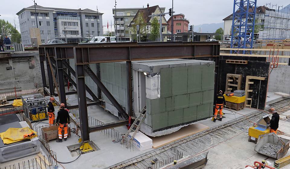 Die Swisscom-Zentrale hängt an einer Stahlkonstruktion auf hydraulischen Stützen. Die Bauarbeiter sind in Stellung, um die Telefonzentrale mithilfe der Hydraulik abzusenken